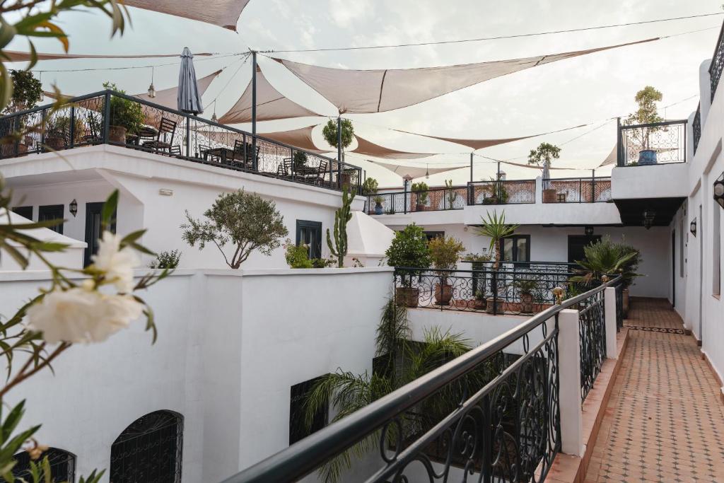 View of the Central House Marrakech Medina, featuring white walls, balconies adorned with plants, and a shaded patio area with seating.
