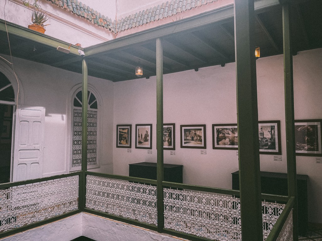 Interior view of the House of Photography museum in Marrakesh, featuring a courtyard surrounded by a decorative railing and framed photographs on the walls.