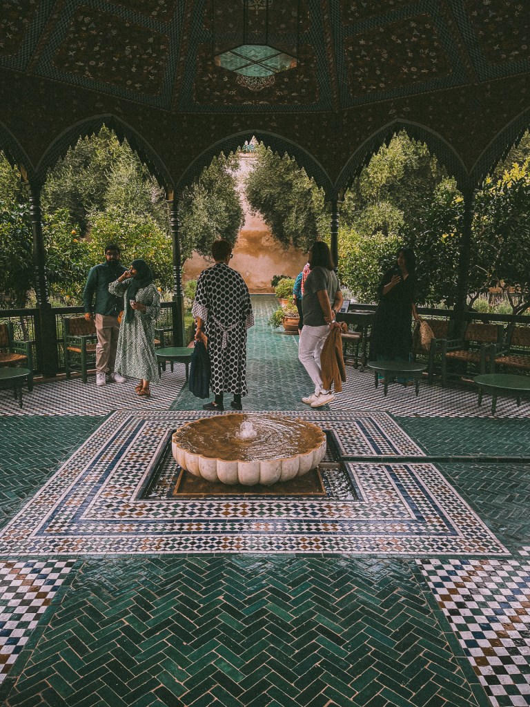 A group of people exploring Le Jardin Secret with intricate tile work and a central fountain, surrounded by lush greenery.