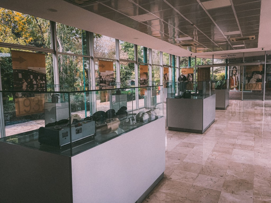 Interior view of the Telecom Museum showcasing historical artifacts and photographs, with glass display cases and natural light coming through large windows.