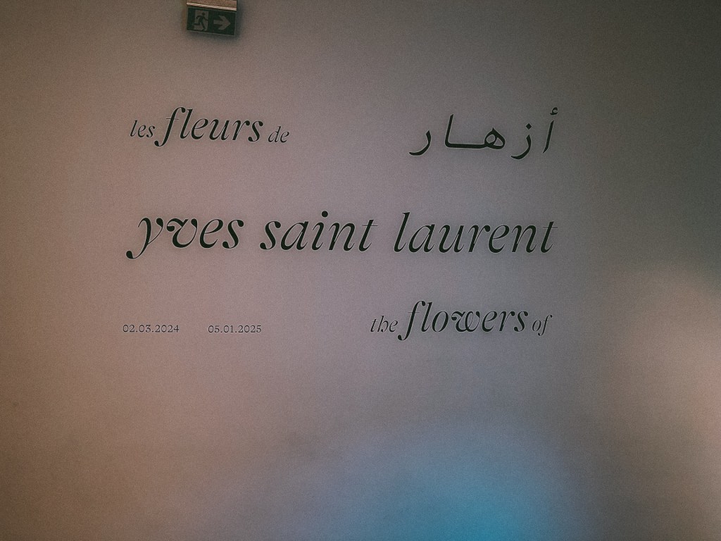 Signage for an exhibition titled 'The Flowers of Yves Saint Laurent' displayed in both French and Arabic, with exhibition dates noted underneath at the Yves Saint Laurent Museum.