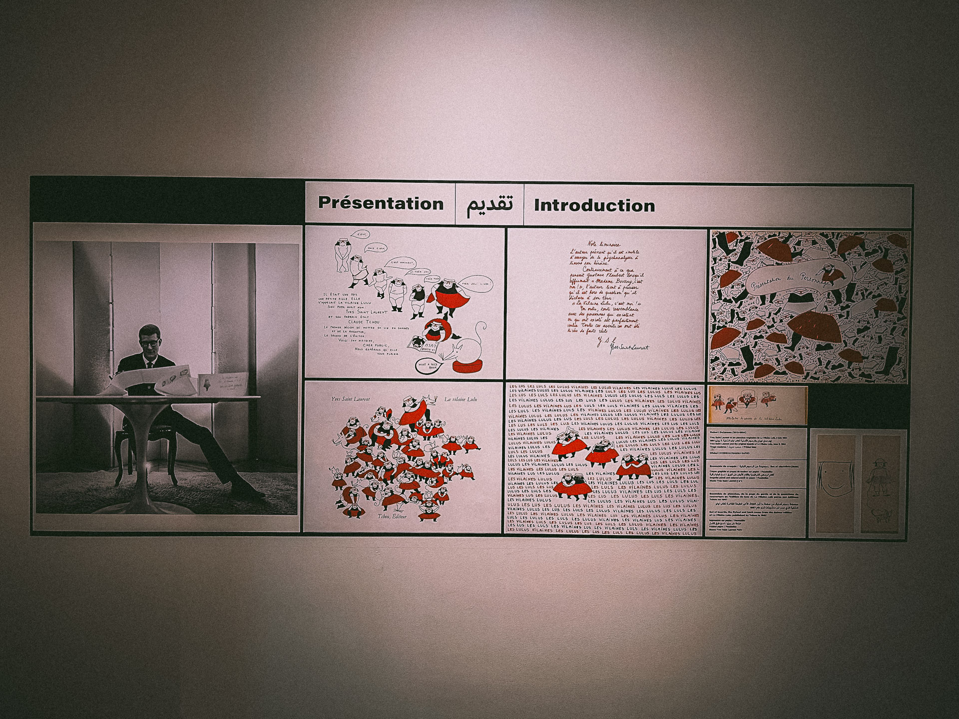 A display wall featuring a black-and-white photo of Yves Saint-Laurent reading a book, accompanied by colorful illustrations and handwritten texts at the Yves Saint Laurent Museum.
