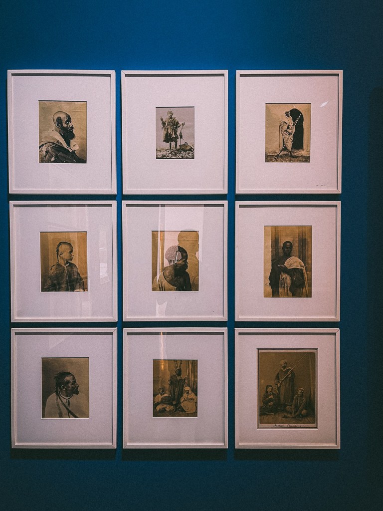 A collage of framed vintage photographs displayed on a blue wall, featuring various portraits and scenes from Moroccan culture at the MACMA Museum.
