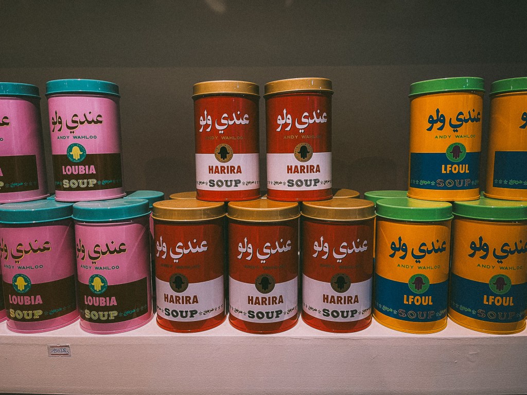 Colorful soup cans labeled with Moroccan soups such as Harira and Loubia, displayed in a neat arrangement at the MACMA Museum. 