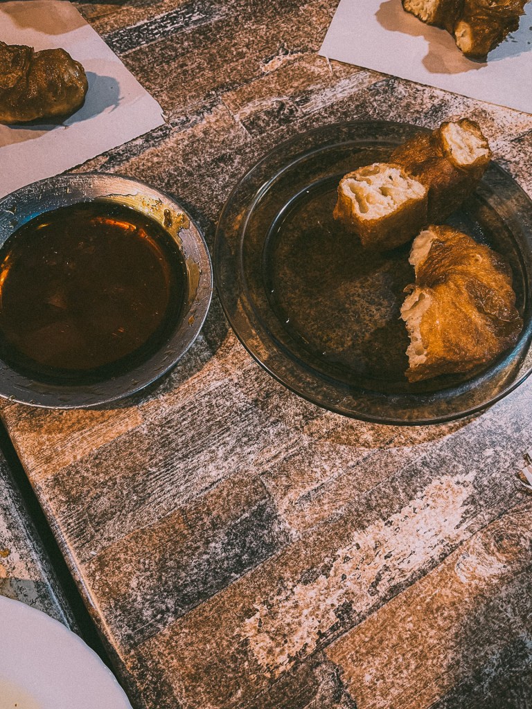 A plate of Moroccan donuts served with a bowl of dipping sauce on a rustic wooden table.