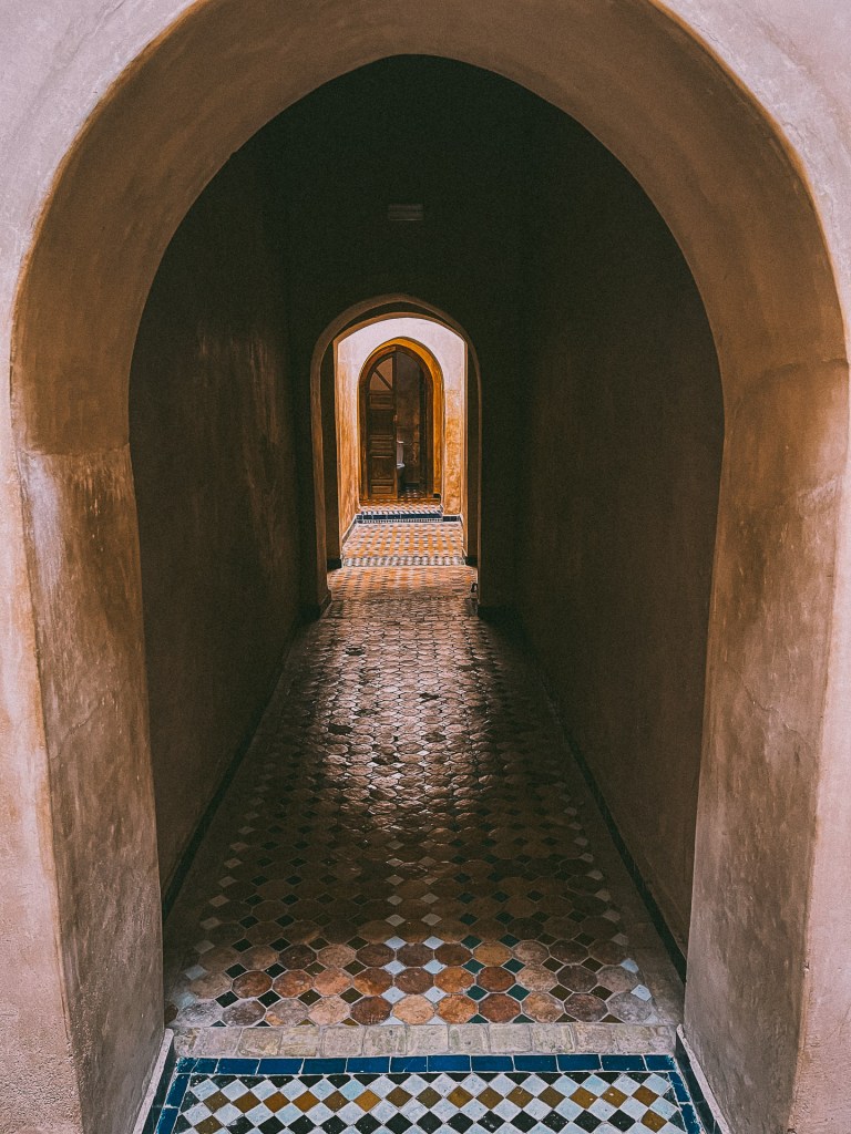 An interior corridor with multiple arched doorways leading to more rooms, featuring colorful tiled flooring and warm earthy walls at the Bahia Palace.